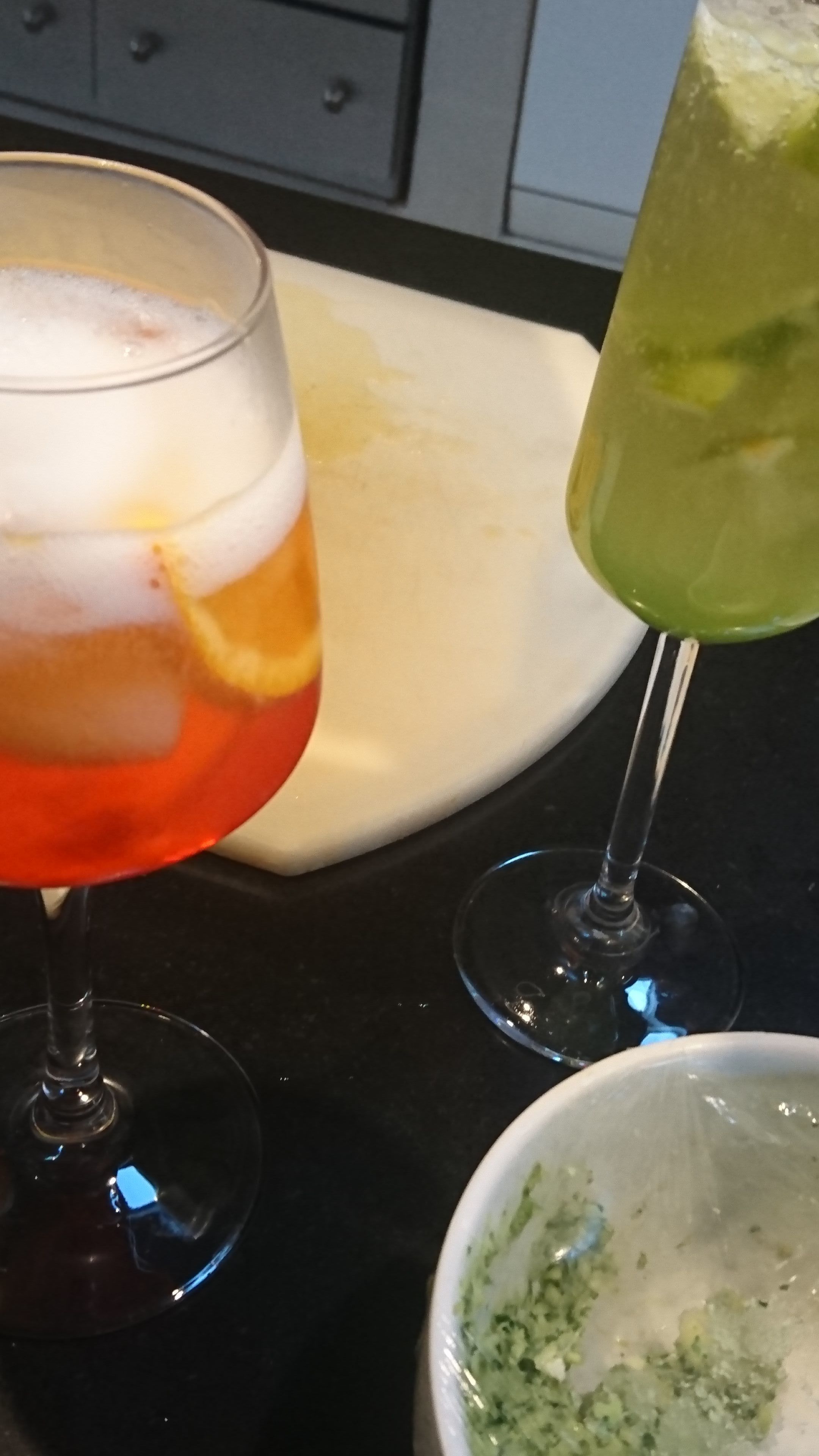 A kitchen counter with two glasses of beverages, one with a red drink and the other with a green drink, and a dirty white plate.