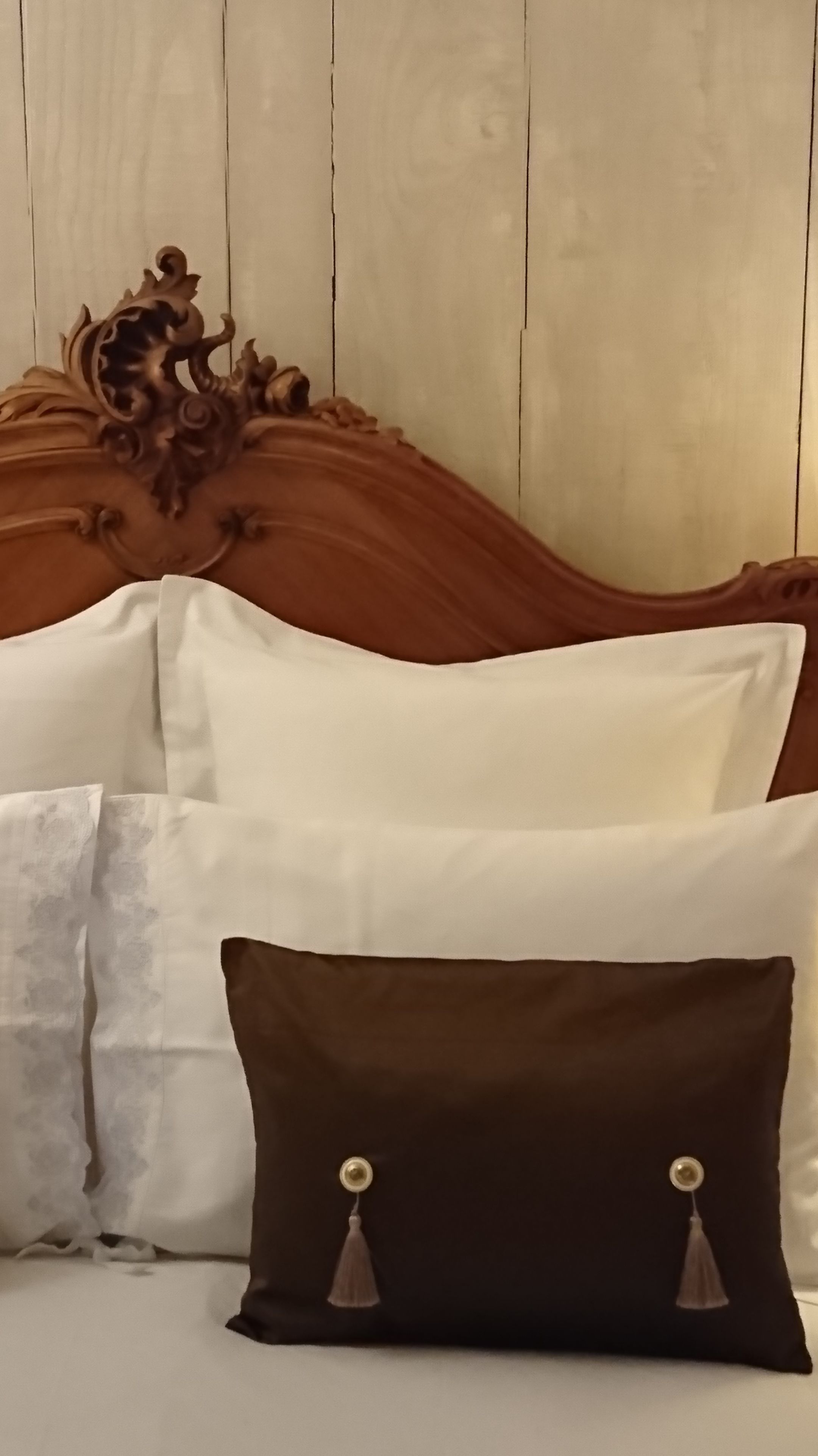 A bed with a wooden headboard, white and brown pillows, and a dark brown pillow with tassels.