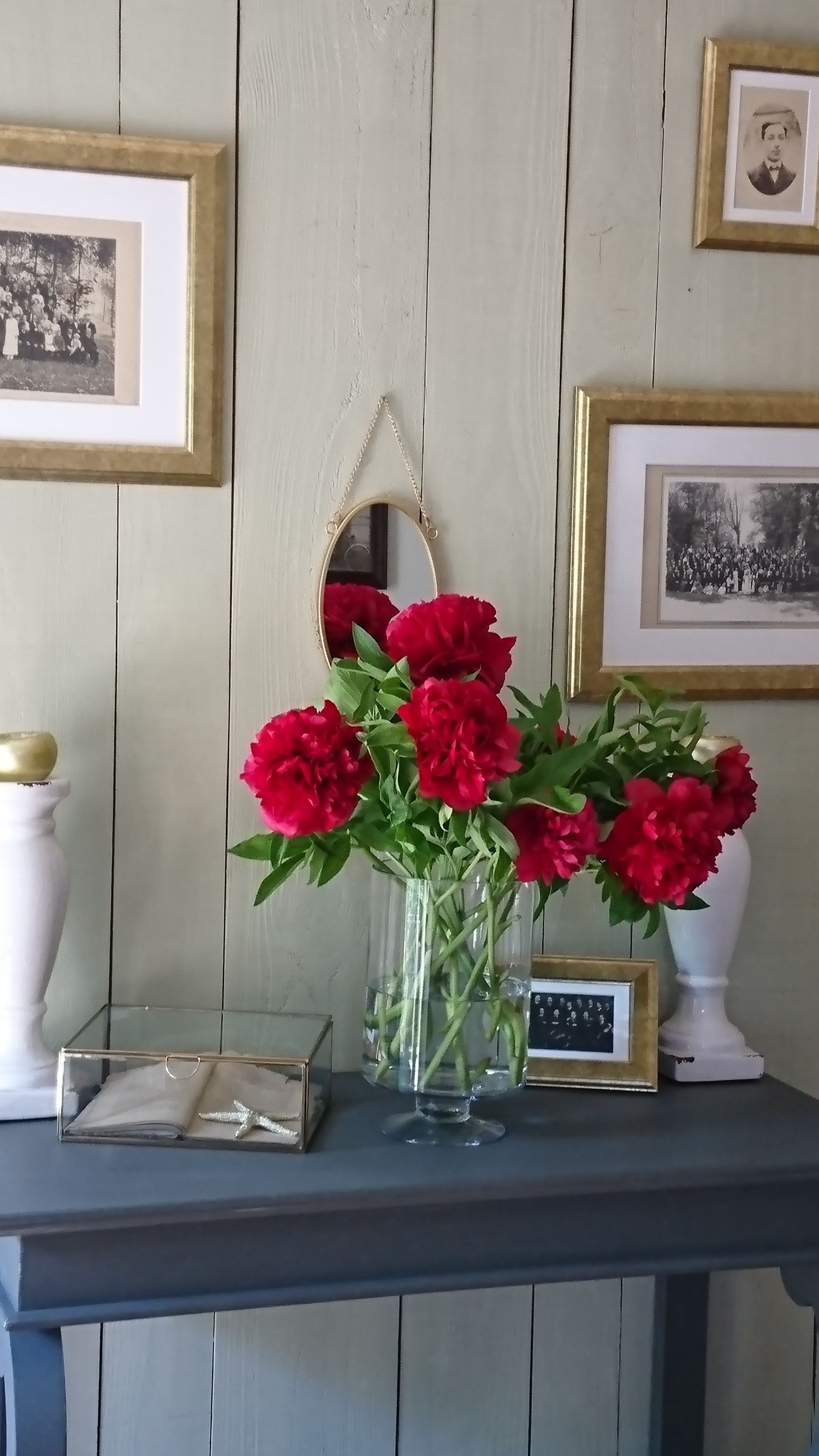 Une table ornée d’un vase de fleurs rouges, d’un petit tableau encadré et d’un miroir décoratif.