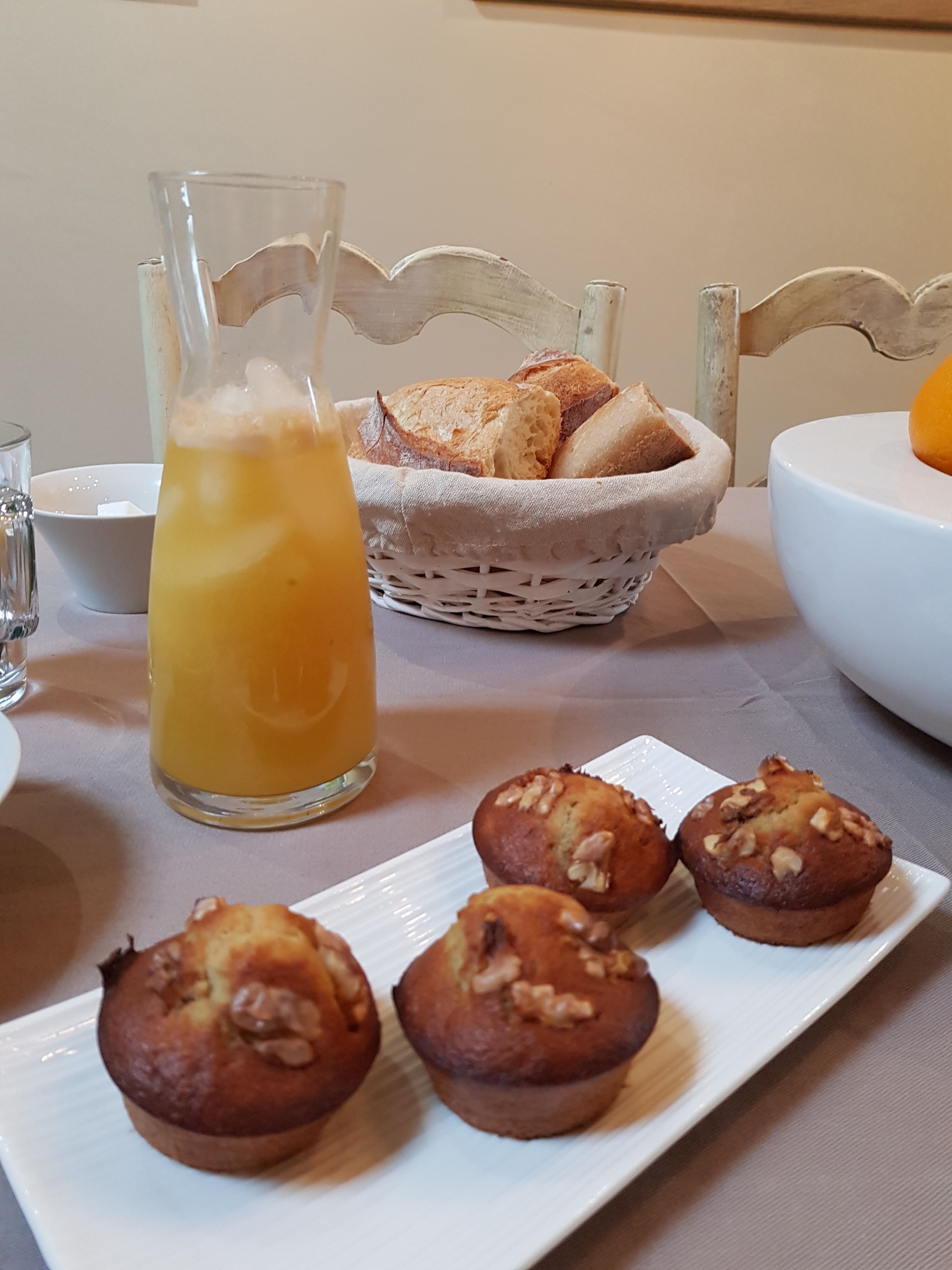 A breakfast setting with a glass of orange juice, a basket of bread, and a plate of muffins.