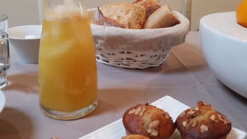 A breakfast setting with a glass of orange juice, a basket of bread, and a plate of muffins.