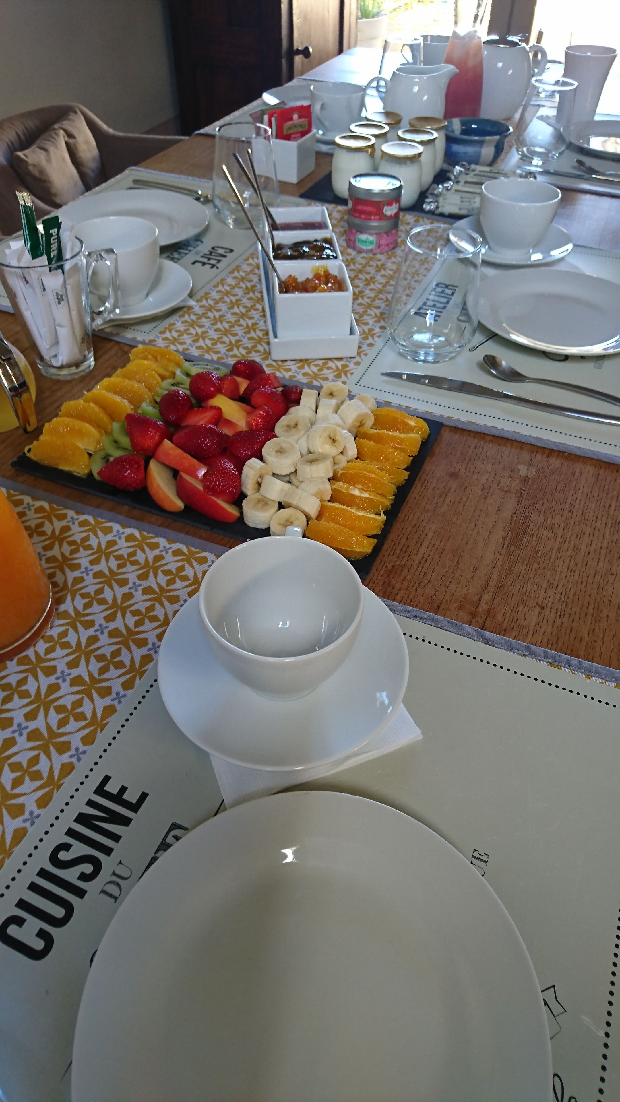 A breakfast setting with a fruit platter, white plates, and a cup of coffee.