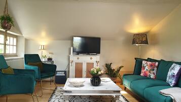 Una sala de estar con sillones color turquesa, una mesa de centro blanca, un televisor sobre un mueble y una lámpara con estampado floral.