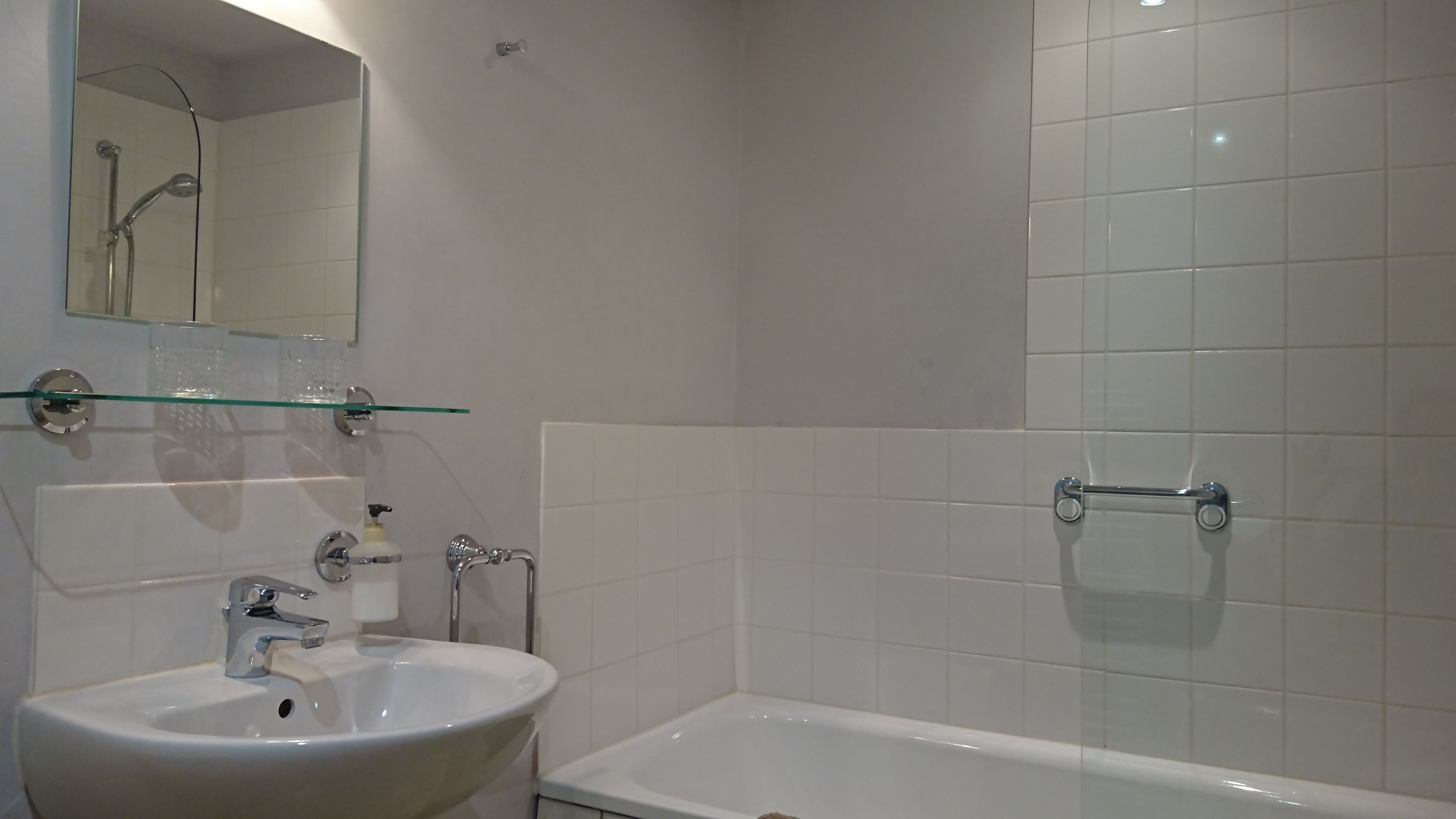 A bathroom with a white sink, a glass shelf, a mirror, and a bathtub.