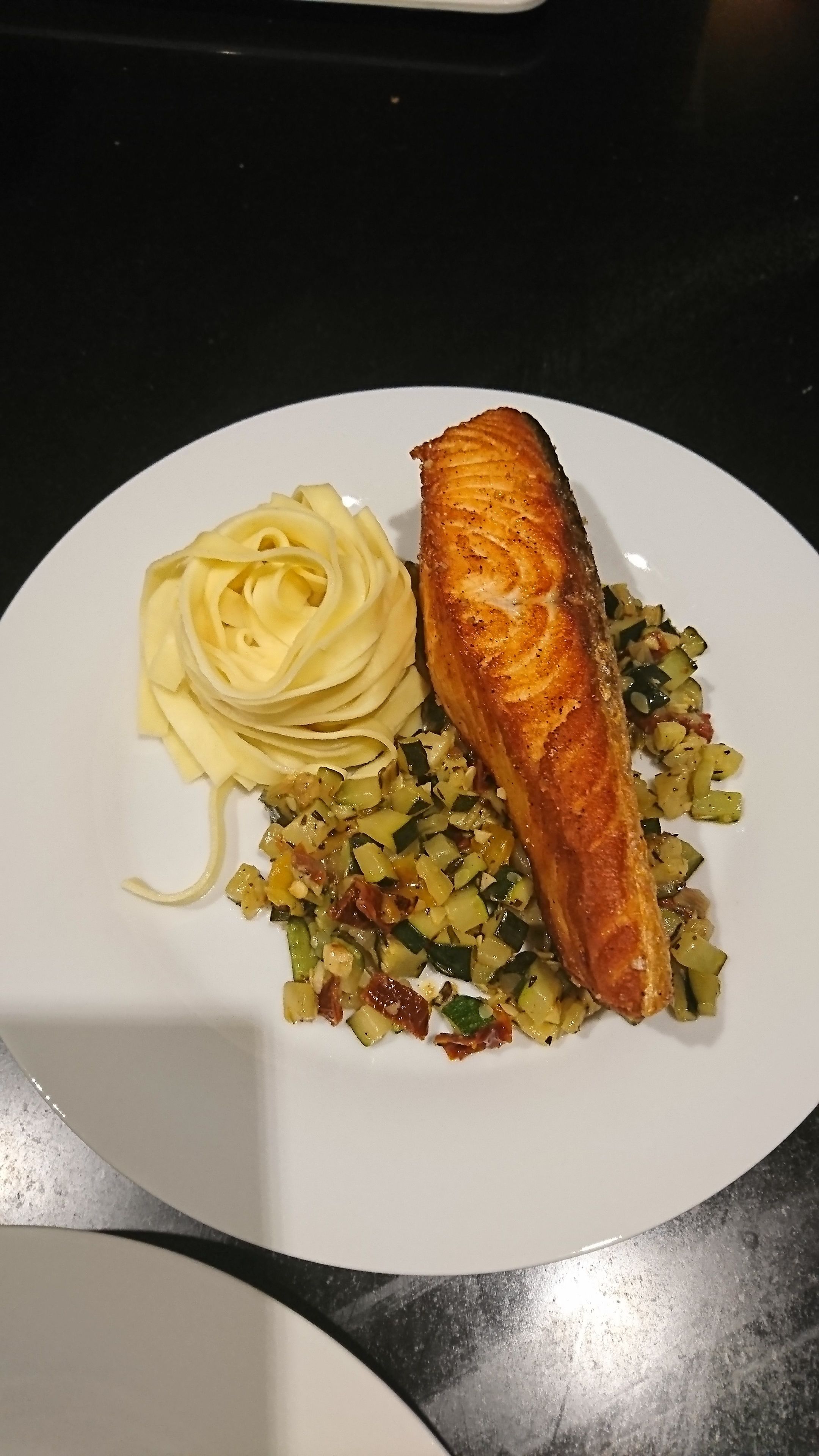 Een bord met een gebakken vis, pasta en een groentemix.