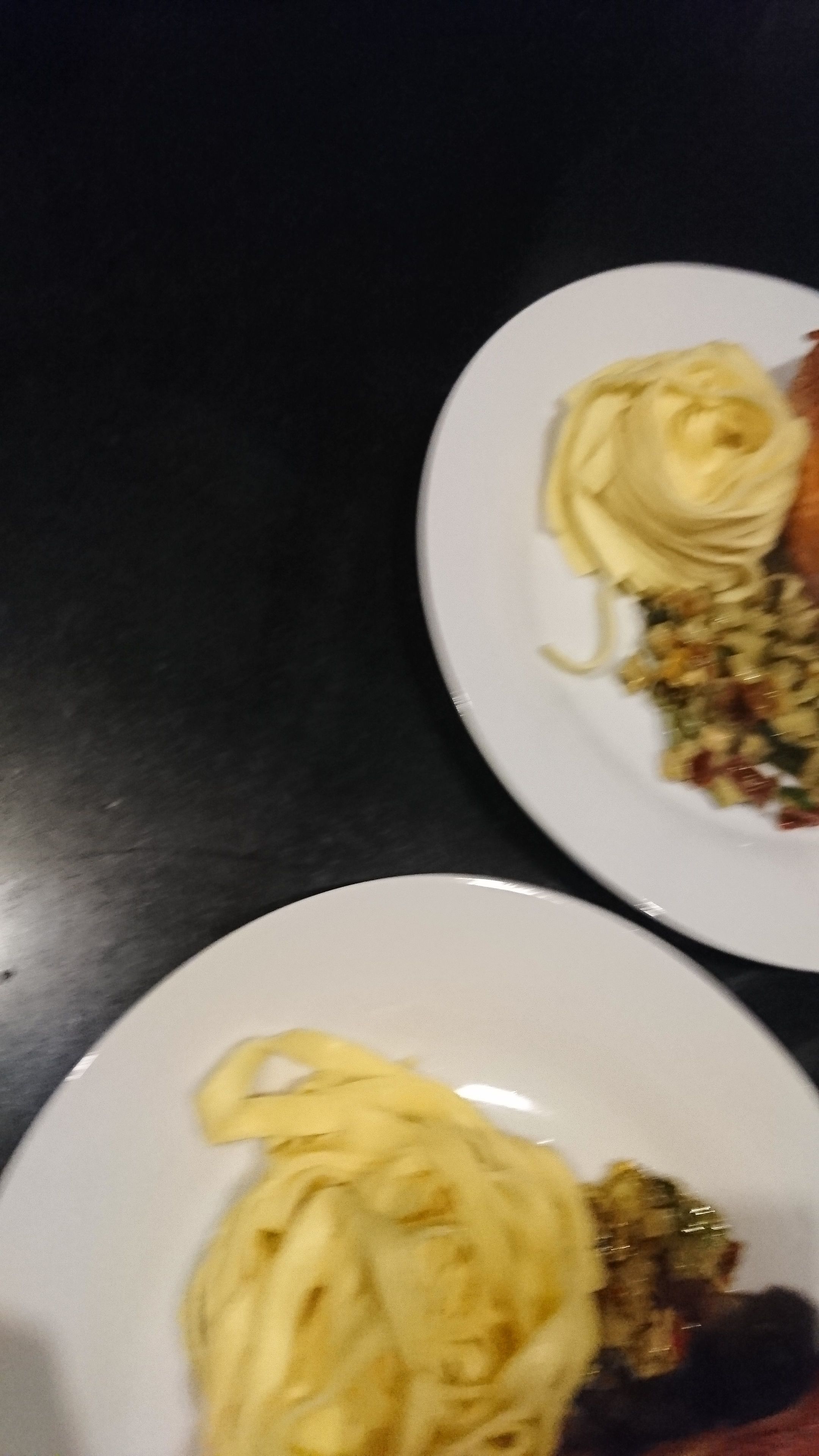 Two plates of food on a dark surface.