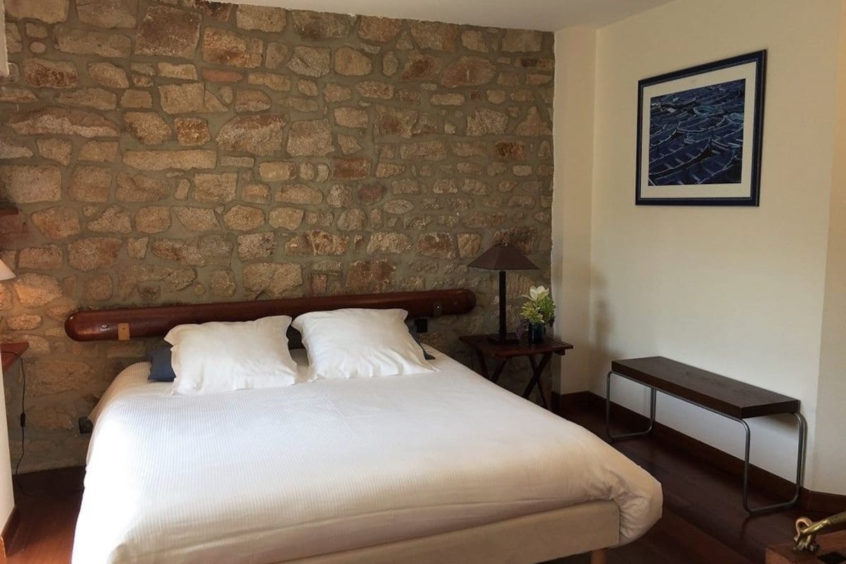 Ein Schlafzimmer mit Steinwand, einem Bett mit weißer Bettwäsche, einem Nachttisch mit Lampe und einem gerahmten Bild an der Wand.