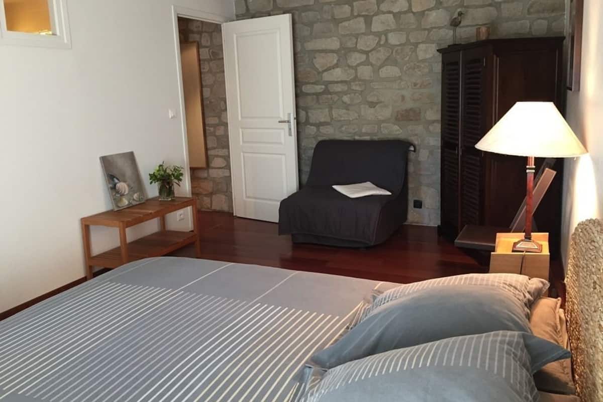 Ein Schlafzimmer mit einem Bett, einem Sessel, einer Lampe und einer Steinwand.