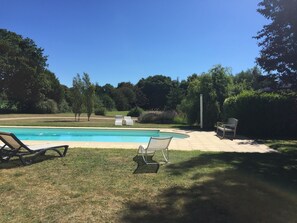 Ein Garten mit Schwimmbad, zwei Liegestühlen, einem Terrassentisch und einer Hecke.