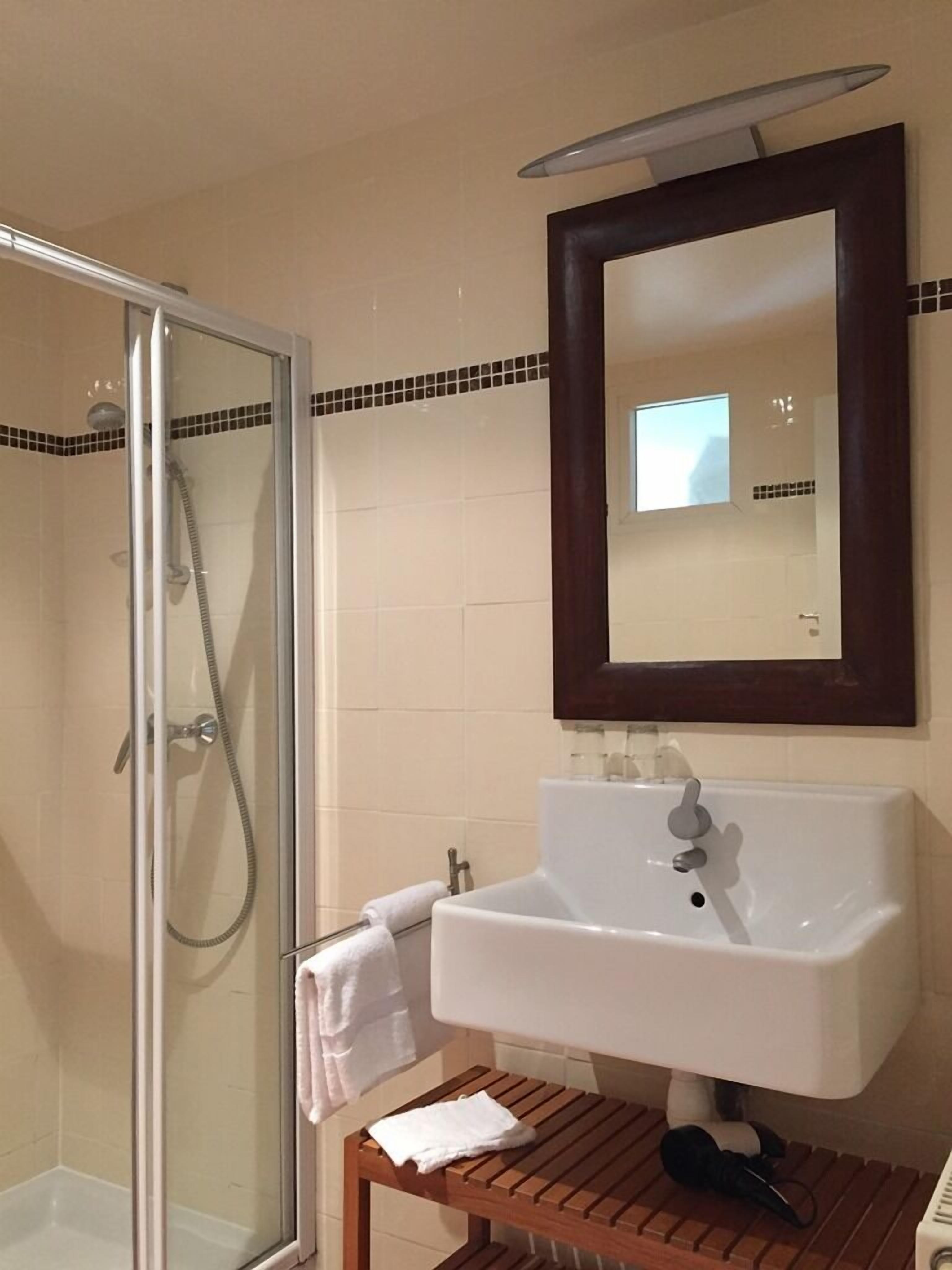 Un baño con ducha de mampara de vidrio, un lavamanos blanco y un mueble de tocador de madera.