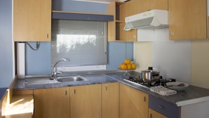 A compact kitchen with wooden cabinets, a sink, a stove, and a window with blinds.