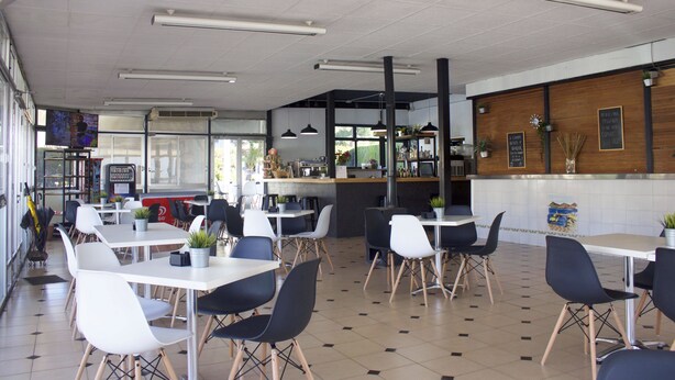 A spacious restaurant with multiple tables and chairs, a counter area, and a view of the outside.