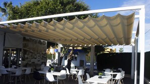 An outdoor seating area with white tables and chairs under a canopy.