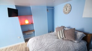 Une chambre à coucher avec un lit, une horloge, un téléviseur et une étagère sur laquelle se trouve une lampe.