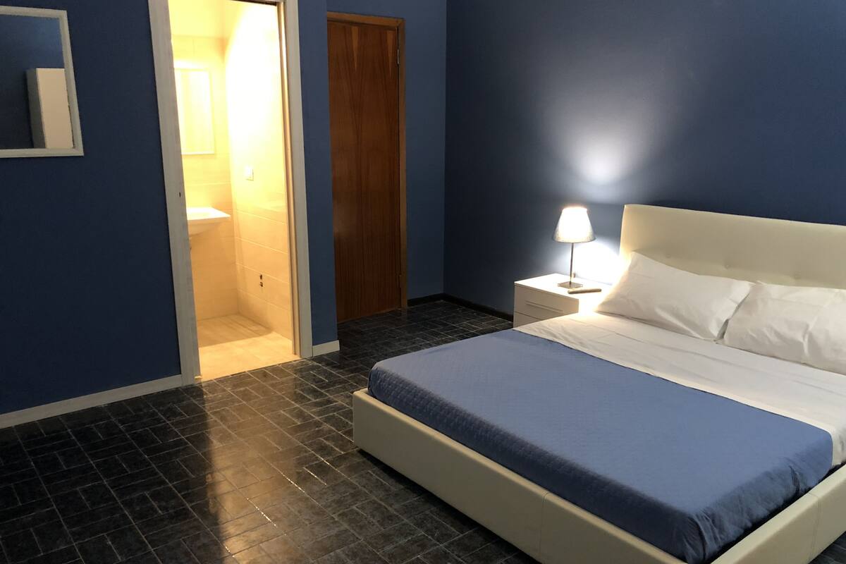 Quarto com cama, mesa de cabeceira e porta para um banheiro.