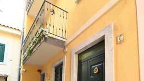 A narrow street with a yellow building, a green door, a small bench, and a staircase leading to an upper floor. - Vico Tauro House (Taormina)