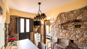 A dining area with a stone wall, a chandelier, and a television. - Vico Tauro House (Taormina)