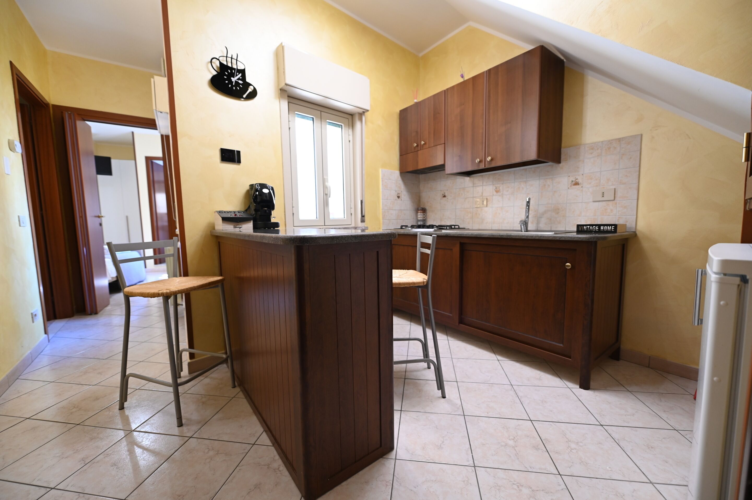 A kitchen with wooden cabinets, a countertop, a sink, and two bar stools.