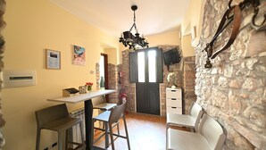 A dining area with a table and chairs, a stone wall, and a television mounted on the wall. - Vico Tauro House (Taormina)
