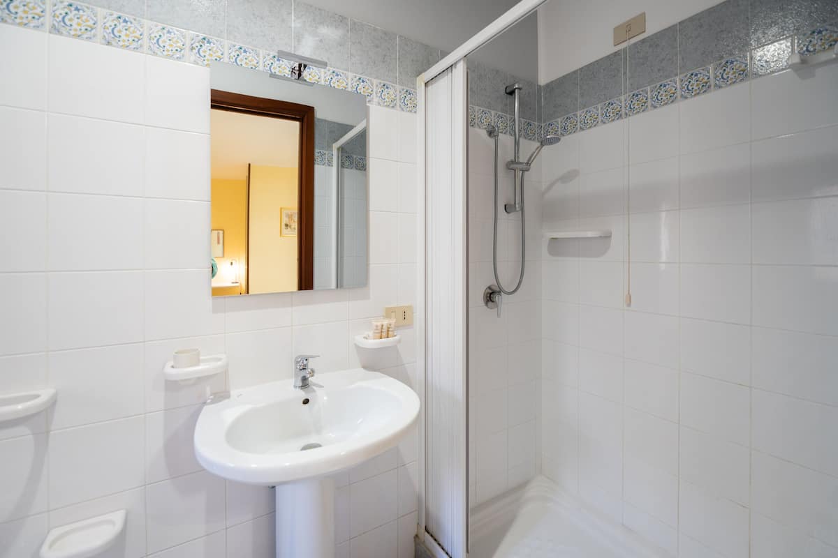 A bathroom with a white sink, a mirror, a shower, and tiled walls.