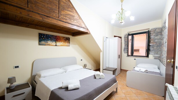 A bedroom with a bed, bedside tables, a nightstand, a painting, a wardrobe, and a window with a stone wall. - Vico Tauro House (Taormina)