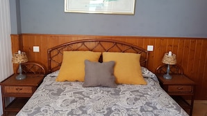 Un dormitorio con cabecera de madera, cama con ropa de cama estampada, dos mesitas de noche con lámparas y un cuadro en la pared.