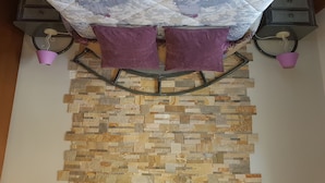 Una habitación con techo estampado, dos cojines morados, una pared de piedra y dos lámparas adosadas a la pared.