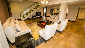 Un salon spacieux doté d’un escalier moderne, d’un téléviseur à écran plat et d’un coin salon confortable avec une table basse.