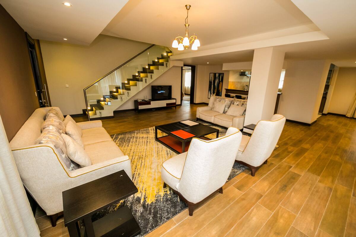 A spacious living room with a modern staircase, a flat-screen TV, and a cozy seating area with a coffee table.