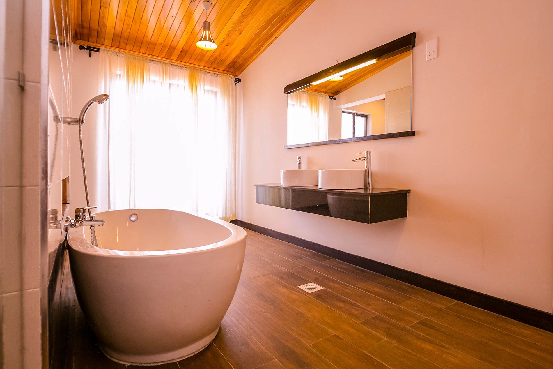 A bathroom with a freestanding bathtub, a wooden ceiling, a large mirror, and a modern sink setup.