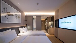Een moderne hotelkamer met twee bedden, een grote spiegel, een televisiescherm waarop 'AccorHotels' staat en een kledingkast.