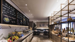 Un hall d’hôtel moderne avec un sol en marbre, un buffet proposant des fruits et des pâtisseries, et un espace détente avec des tables et des chaises.