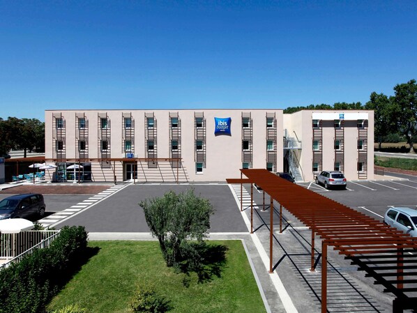 A modern hotel with a central entrance, multiple floors, and a parking area. - ibis budget Manosque Cadarache (Manosque)