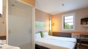 Habitación de hotel con cama, escritorio, televisión y baño con lavamanos.