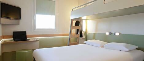 A hotel room with a bunk bed, a desk with a laptop, a television mounted on the wall, and a window providing natural light.