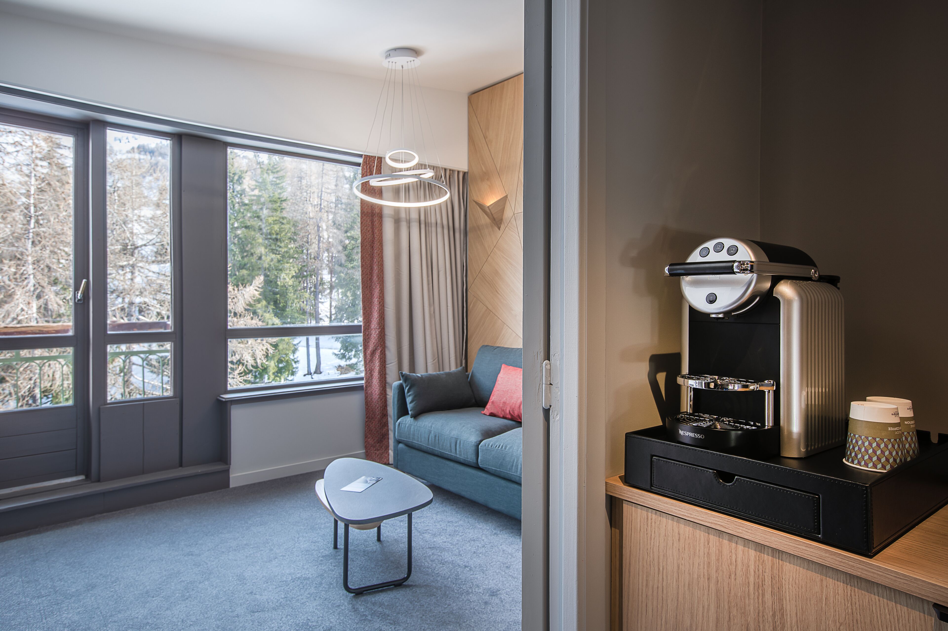 Une chambre moderne dotée d’une grande fenêtre, d’un canapé, d’une petite table et d’une machine à café.
