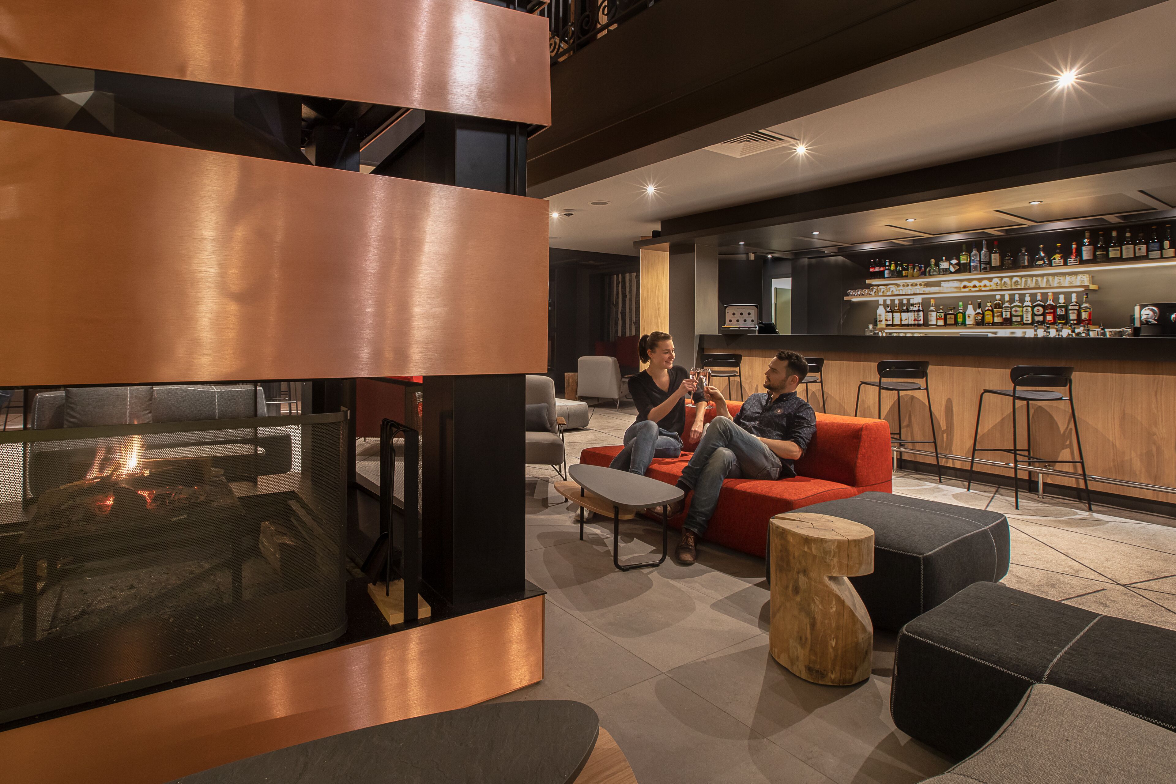 A modern lounge area with a fireplace, seating, and a bar with various bottles.