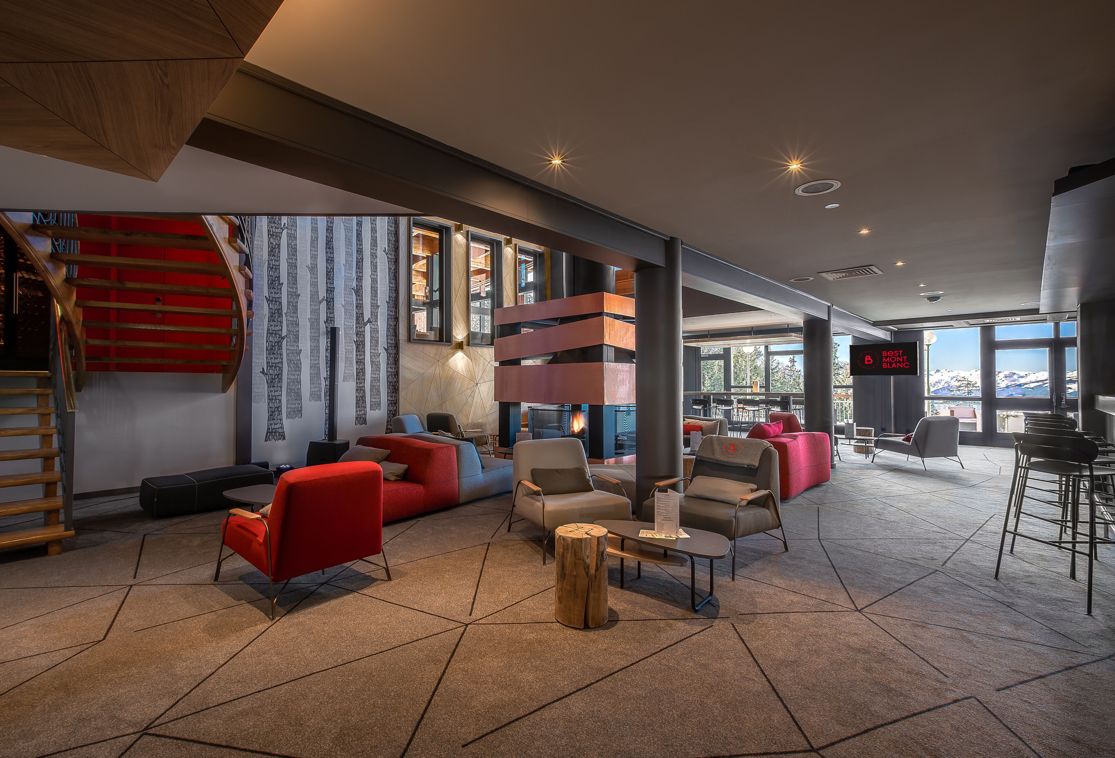 A modern lobby with a staircase, seating areas, and a large window offering a view.