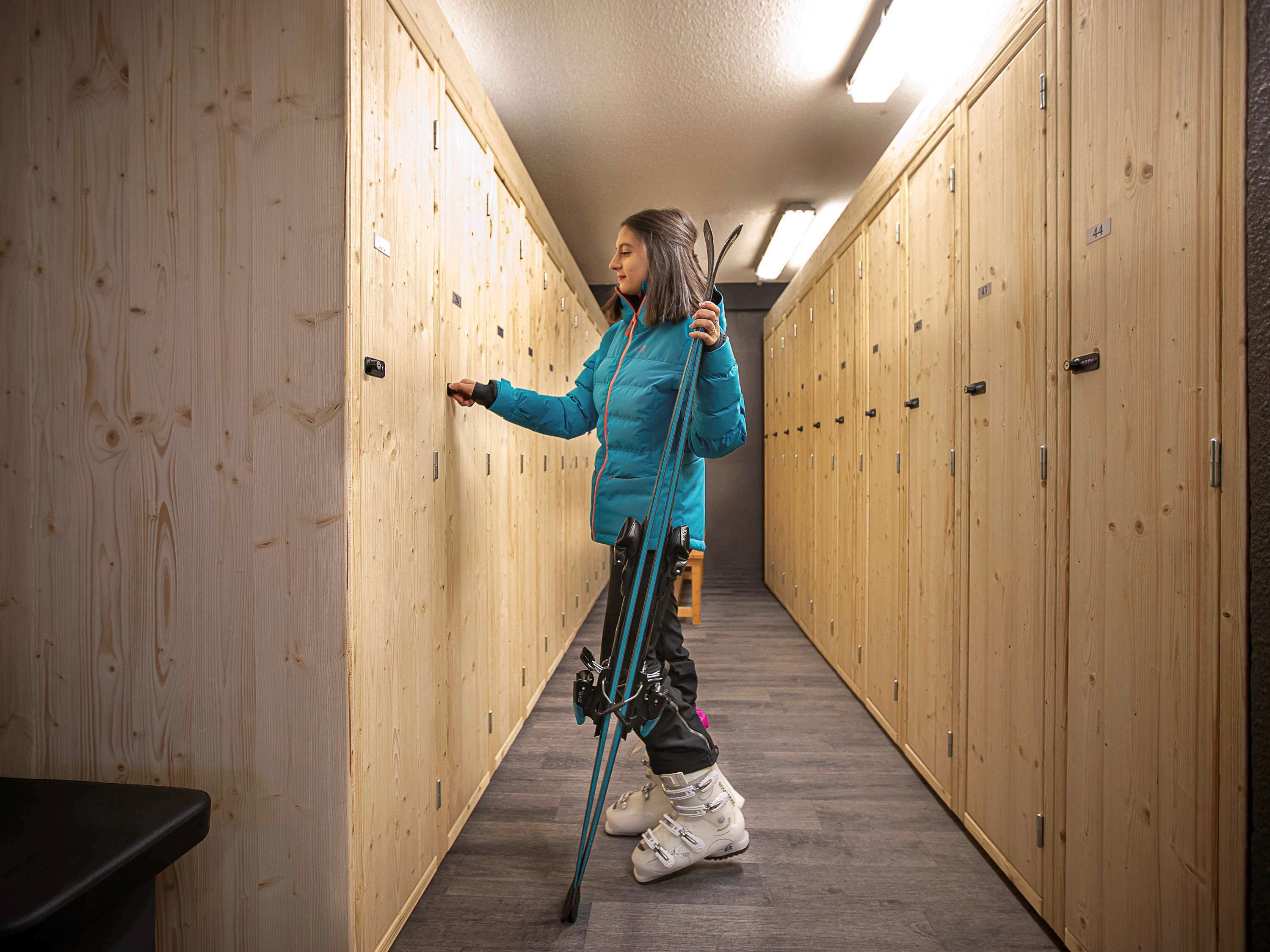 A person in a blue jacket and white boots standing in a hallway with wooden lockers.