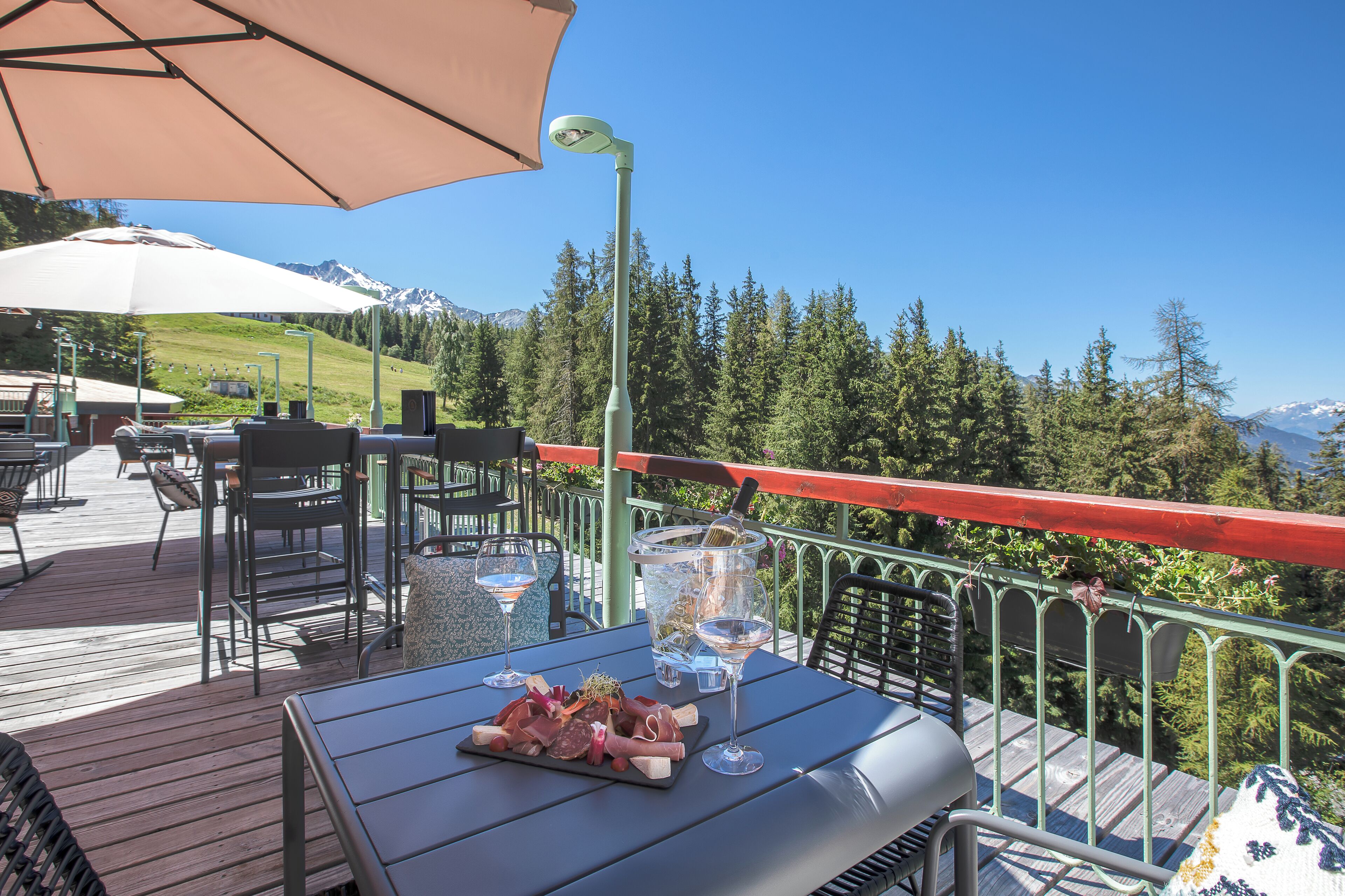 An outdoor dining area with a view of mountains, a grill, and a table set with food and drinks.