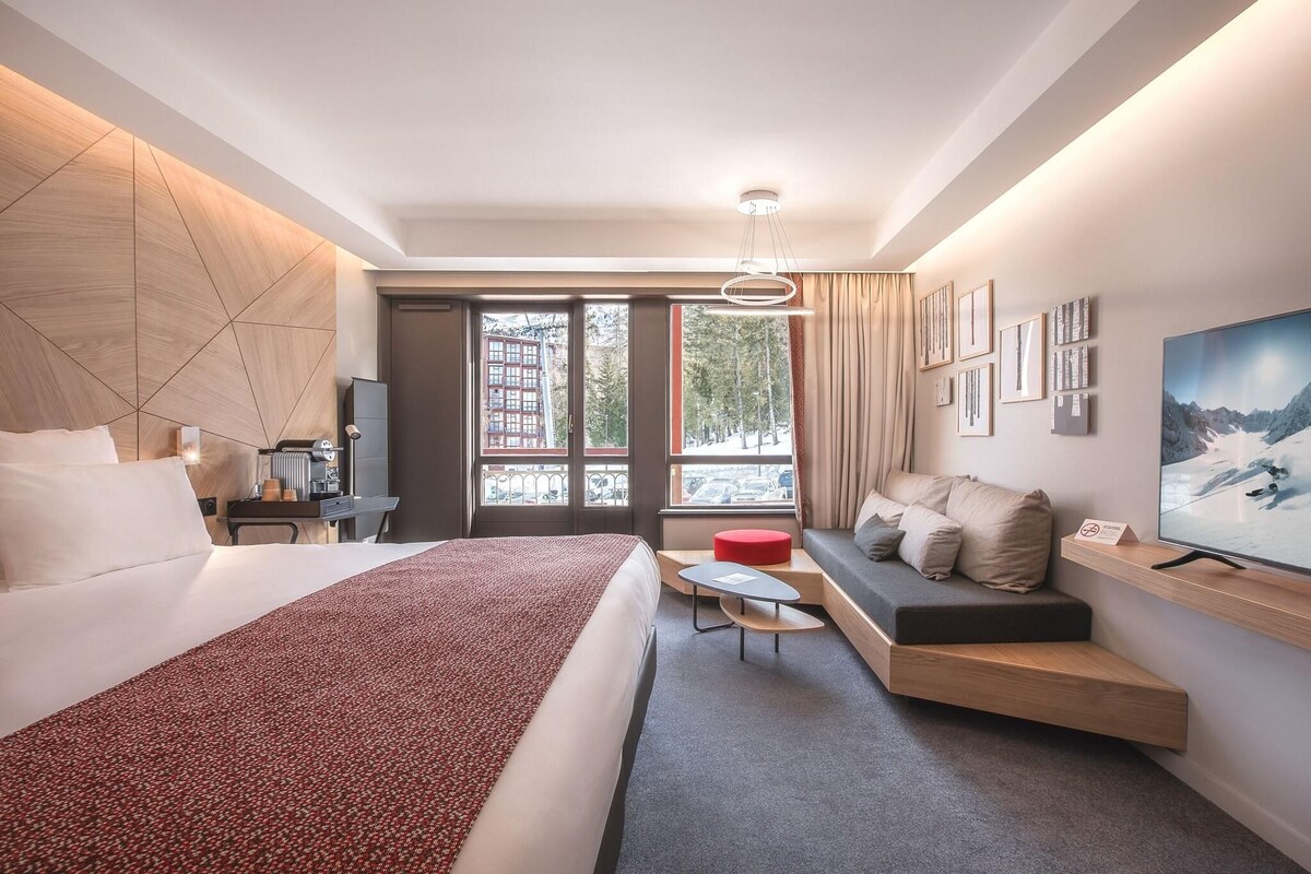 Una habitación de hotel moderna con una cama, un sofá, un televisor y vistas a un paisaje nevado.