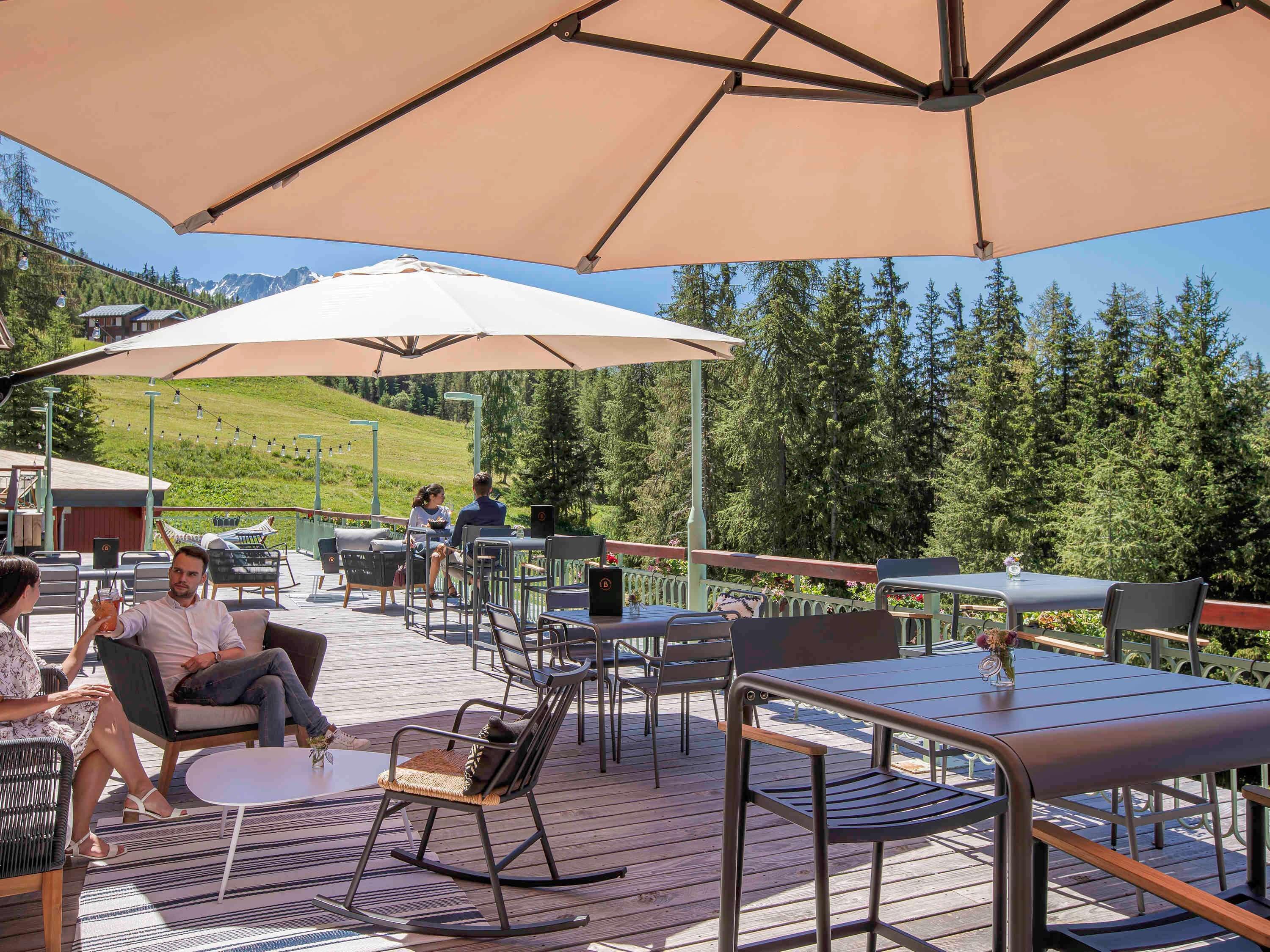 Un patio al aire libre con mesas y sillas, una terraza de madera y vistas a un paisaje montañoso.