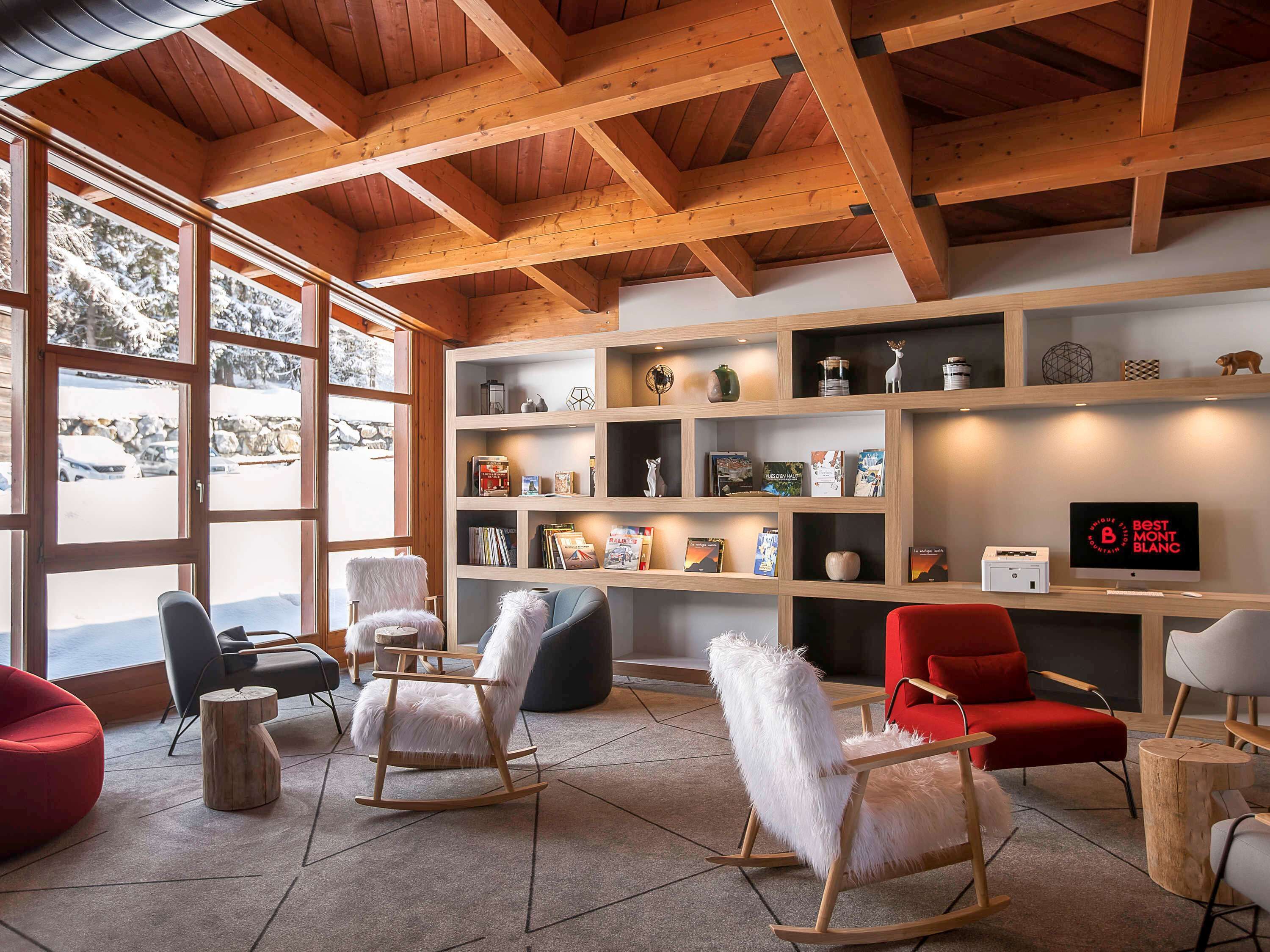 Un interior moderno con vigas de madera, una estantería y varias mecedoras.