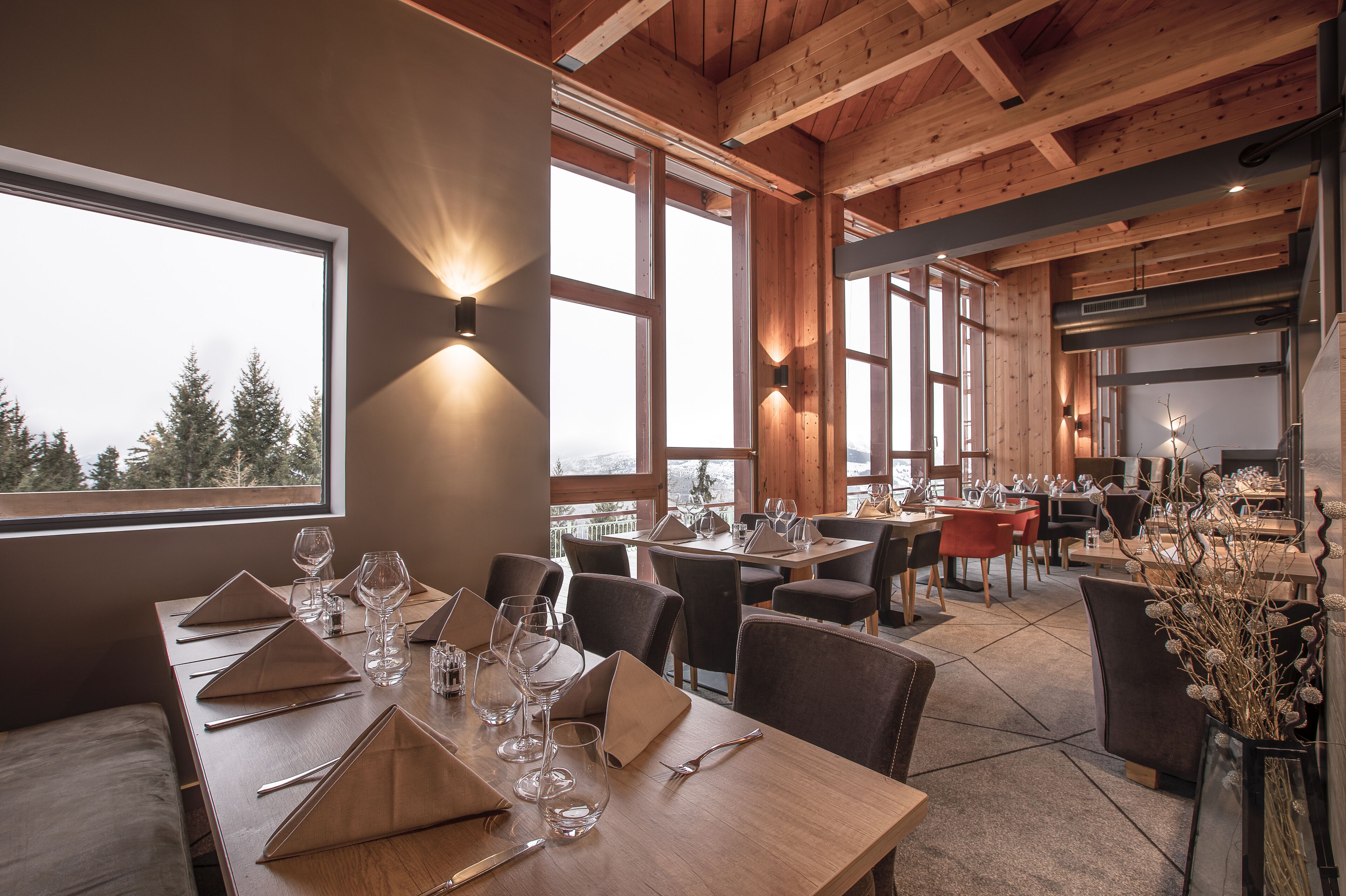A restaurant with wooden beams, large windows, and tables set for dining.