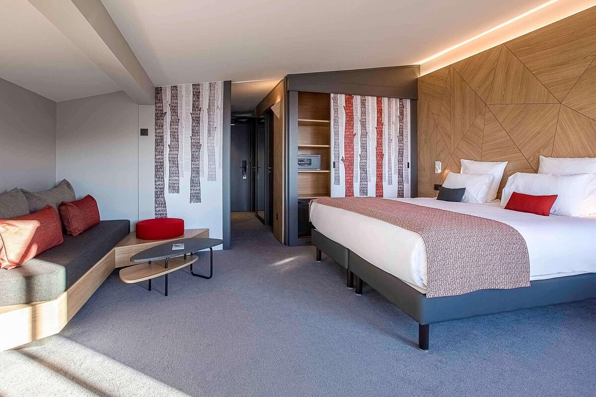 A modern hotel room with a bed, a sofa, a small table, and a walk-in closet.