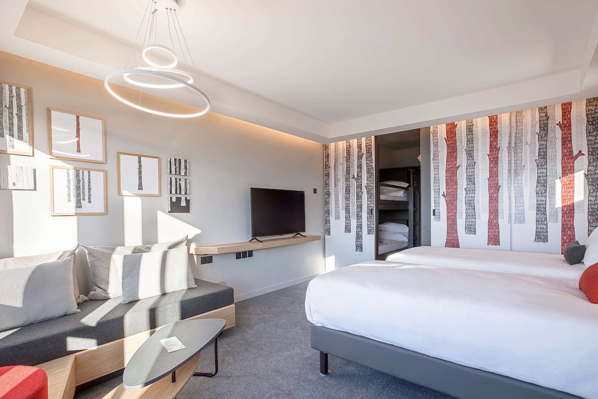 A modern hotel room with a bed, a desk, a sofa, a TV, and a wardrobe.