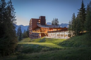 A modern building with a glass facade, surrounded by trees and mountains. - Altezza Arc 1800 Hôtel & Spa (Bourg-Saint-Maurice)