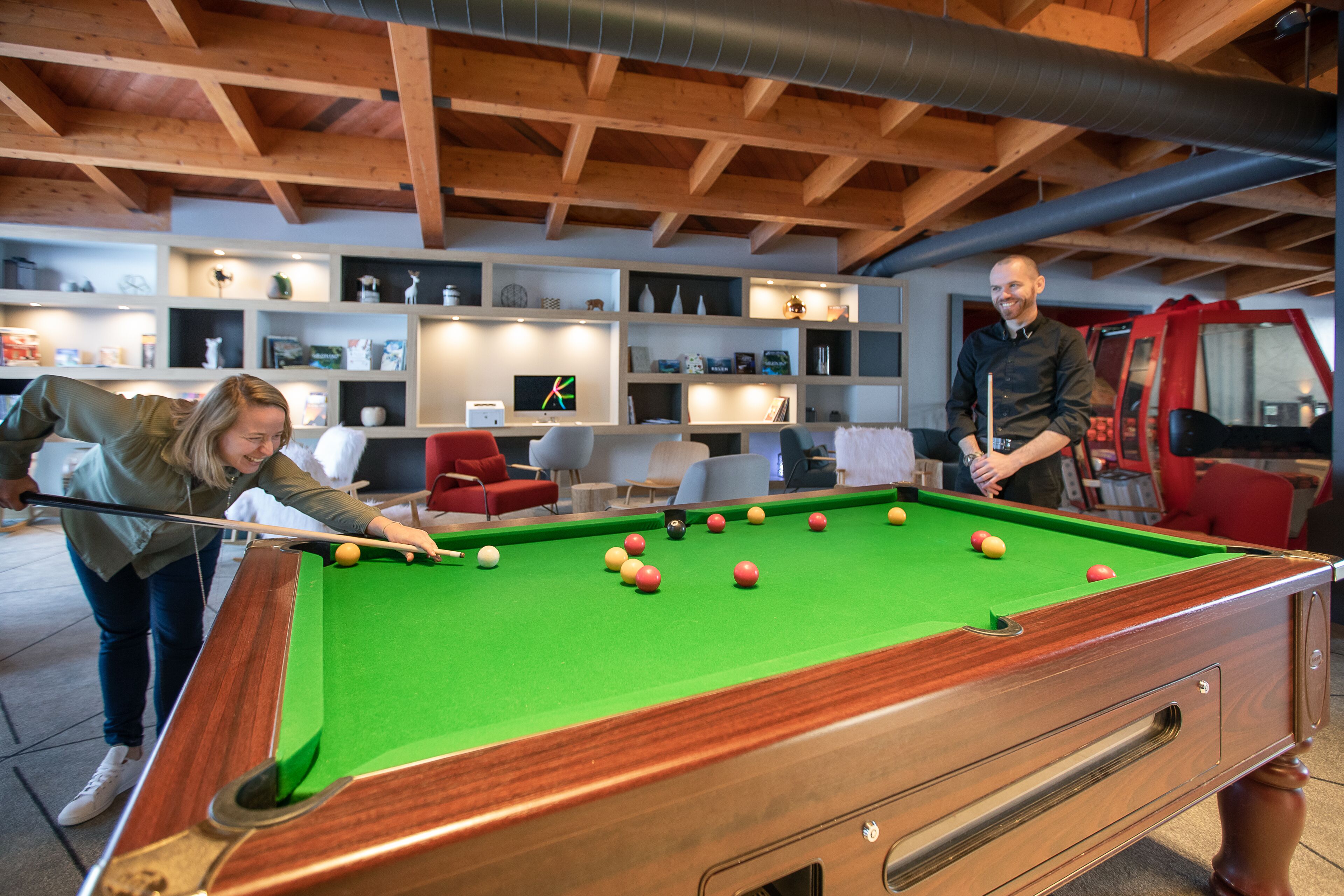 A pool table in a room with wooden beams on the ceiling and shelves with various items.