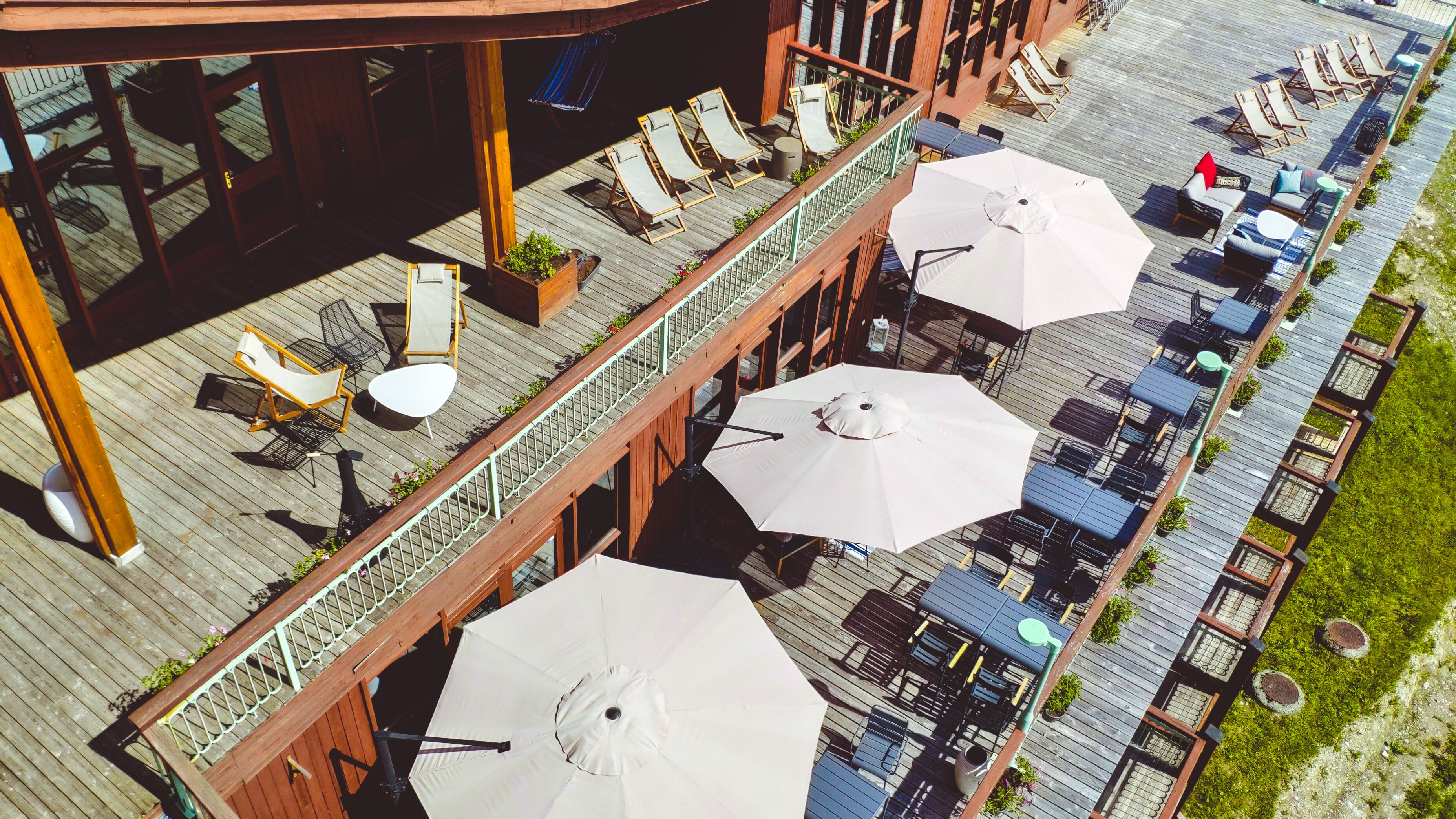 A wooden deck with outdoor seating, including lounge chairs and tables, and umbrellas providing shade.