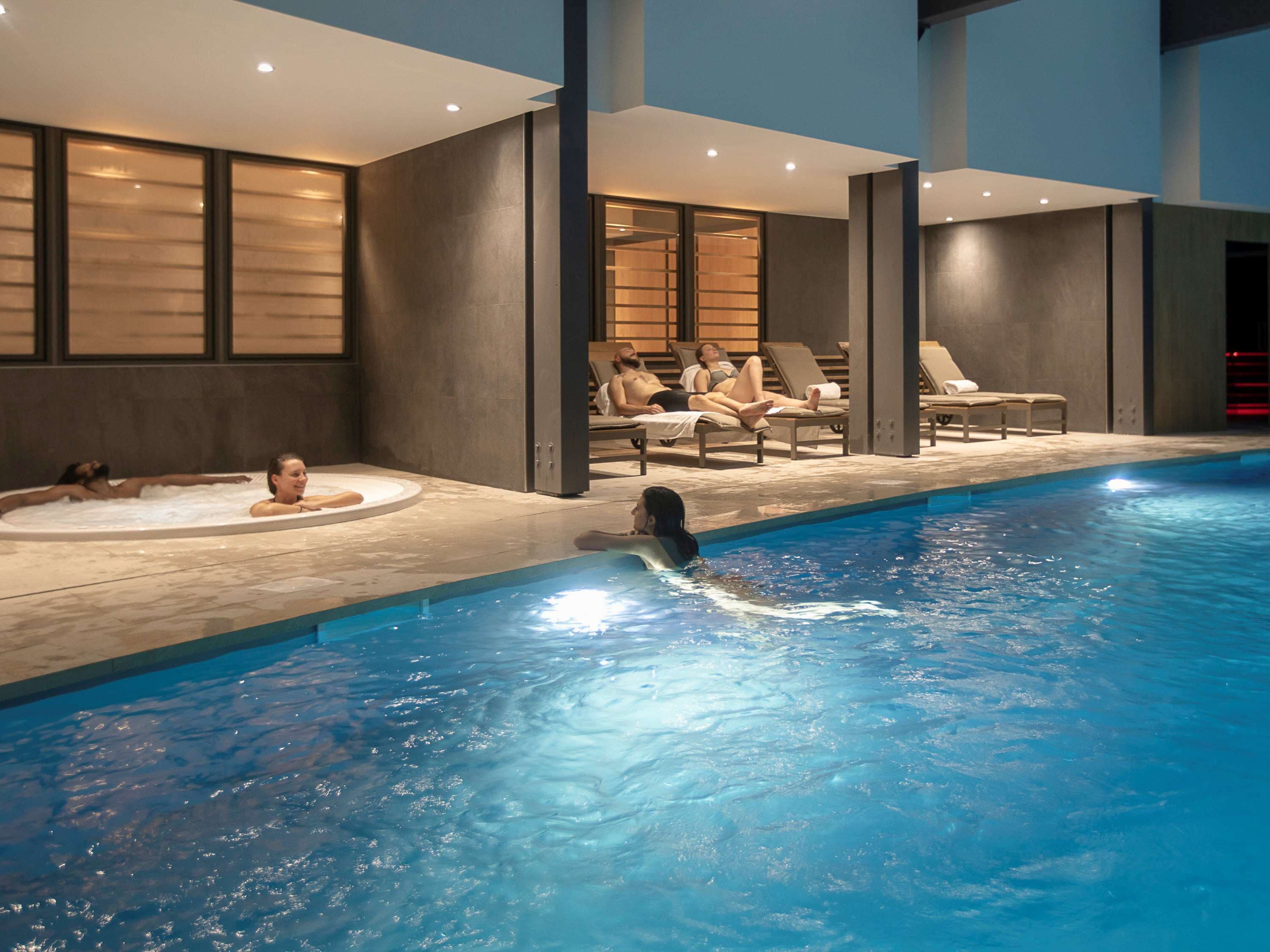 An indoor swimming pool with lounge chairs and a hot tub area.